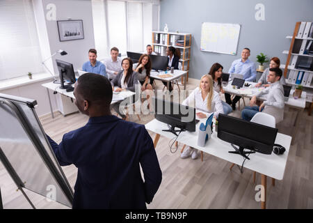 Rear View Of An African Male Giving Presentation To His Colleague In Office Stock Photo