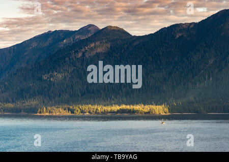 Small fishing troller in distance below mountains, early morning in Clarence Strait, North of  Ketchikan, Alaska. Stock Photo