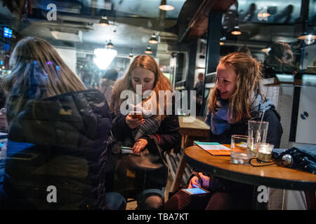 Oxford, United Kingdom - Mar 3, 2017: View from the street through transparent glass of cafe of young girls having a coffee in central Oxford one of the girl using Stock Photo