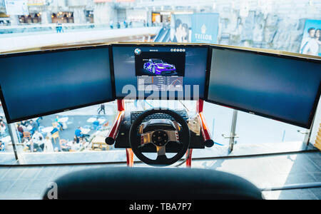 Bucharest, Romania - 2016: Triple screen setup with steering wheel and pedals installed on racing chair inside Bucharest Mall - Racing games for customers Stock Photo