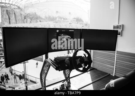 Bucharest, Romania - 2016: Triple screen setup with steering wheel and pedals installed on racing chair inside Bucharest Mall - Racing games - black and white image Stock Photo