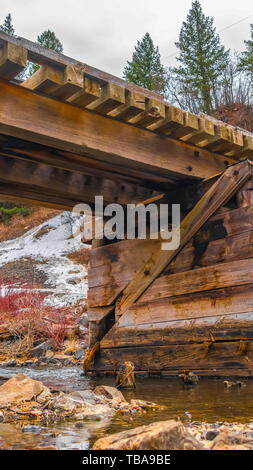 frame Vertical Rustic wooden bridge crossing over a rocky stream with clear shallow water Stock Photo