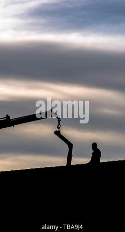 frame Vertical Silhouette of a lifting crane and a man standing on the roof Stock Photo