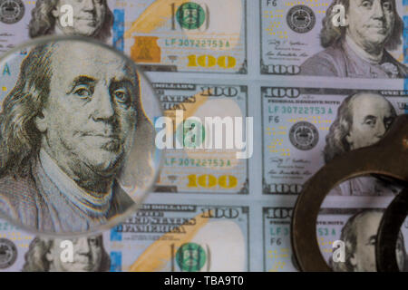 100 US dollars banknotes under magnifying glass of counterfeit money and police handcuffs Stock Photo