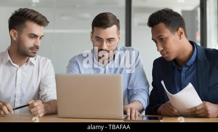 Serious male employees work on laptop together at meeting Stock Photo