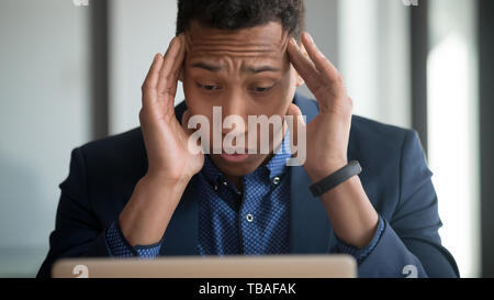 Tired african American employee suffering from headache using laptop Stock Photo