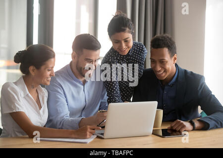 Smiling diverse employees laugh cooperating at laptop in office Stock Photo