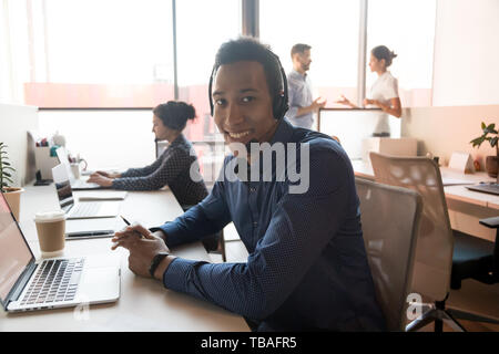 Portrait of smiling ethnic male agent in headset at workplace Stock Photo