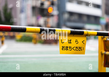 Tokyo, Japan Shibuya street sidewalk road by buildings during day with railroad crossing and closed gate sign translation for please wait a while Stock Photo