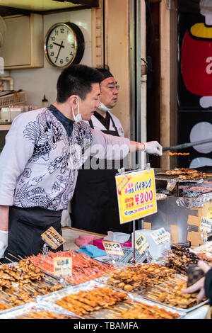 Tokyo, Japan - March 30, 2019: Outer market in Tsukiji near Ginza with grilled fish vendor on street and sign Stock Photo