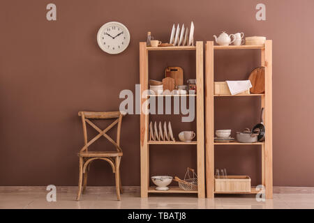 Set of clean dishes with utensils on wooden shelves near color wall Stock Photo