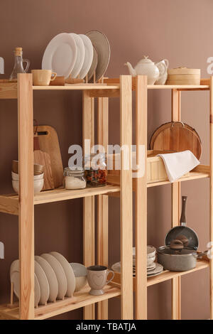 Set of clean dishes with utensils on wooden shelves near color wall Stock Photo