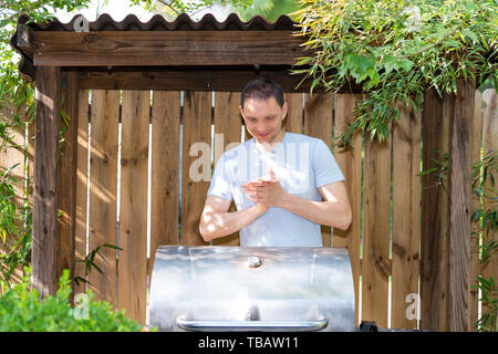 Barbeque bbq modern new grill in outdoor nature summer backyard garden on sunny day with man standing getting ready happy Stock Photo