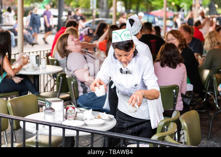New Orleans, USA - April 23, 2018: Waitress woman cleaning up with people sitting at table at Cafe Du Monde eating beignet sugar donuts