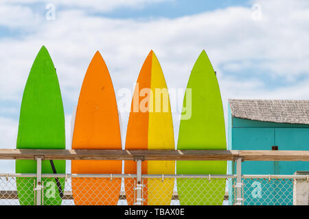 Stack row of multicolored colorful stand up surfing boards on railing fence with green orange and yellow color against blue sky lifeguard tower or ren Stock Photo