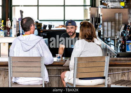 Destin, USA - April 24, 2018: Inside of Margaritaville restaurant with mature couple sitting at bar counter, bartender serving alcoholic drink in Harb Stock Photo