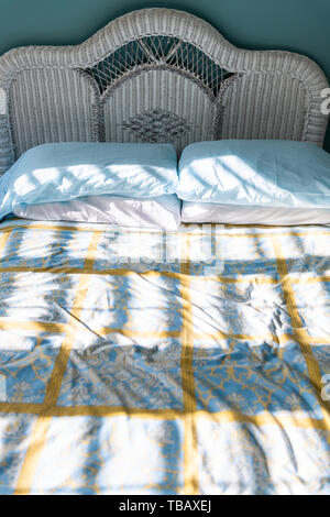 Closeup of new clean bed comforter with wicker rattan headboard vintage beach blue green pillows in sunny bedroom in home, house or apartment Stock Photo