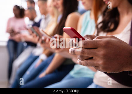 Multi-ethnic Young People Leaning Near Table In Row Using Smartphone Stock Photo