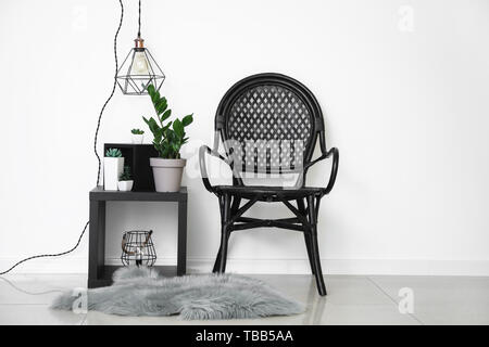 Wicker chair with plants in pots and new lamp near white wall Stock Photo