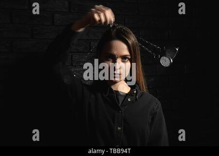 Female hypnotist with swinging pendulum on dark background Stock Photo
