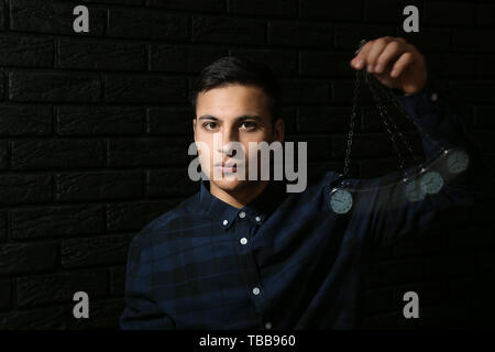 Male hypnotist with swinging pendulum on dark background Stock Photo