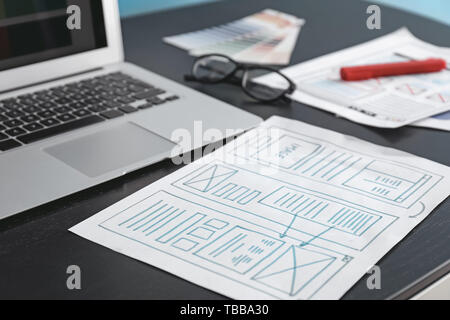Modern laptop and sheet of paper with drawn wireframe on table of IT designer in office Stock Photo