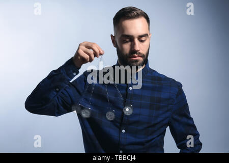 Male hypnotist with swinging pendulum on grey background Stock Photo