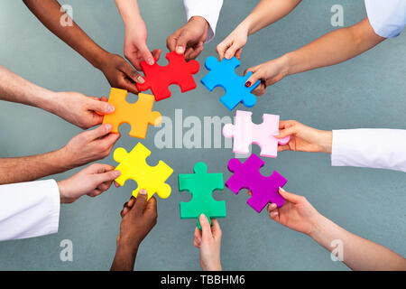 High Angle View Of Medical Team Solving Colorful Jigsaw Puzzle Against Grey Background Stock Photo