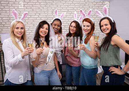 Portrait Of Smiling Young Women Enjoying Drinks Looking At Camera Against Brick Wall Stock Photo