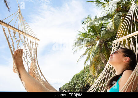 Smiling Young Woman Lying On Hammock Looking Up In The Sky At Beach Stock Photo