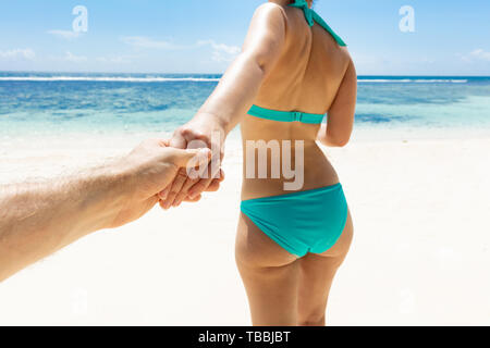 Close-up Of Woman In Bikini Holding The Hand Of Her Boyfriend On Beach Stock Photo