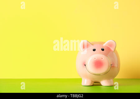 Happy piggy bank on color table against yellow background, space for text. Finance, saving money Stock Photo