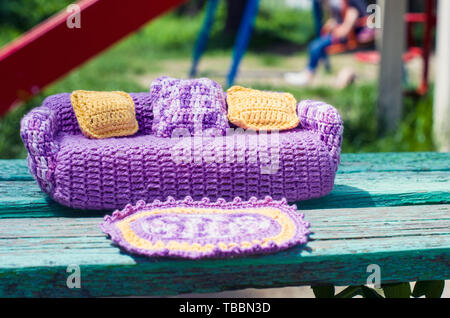 Crocheted violet sofa for dolls with yellow and melange pillows and a rug. Handmade toy furniture Stock Photo