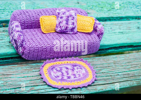 Crocheted violet sofa for dolls with yellow and melange pillows and a rug. Handmade toy furniture Stock Photo