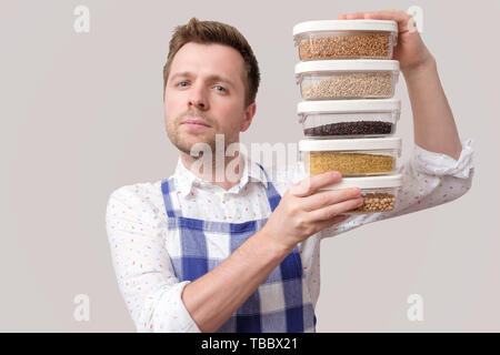 Young smiling man in apron hold several boxes with grains. Stock Photo