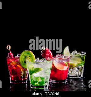 Four colorful tasty alcoholic cocktails in a row at the bar stand. Luxury vacation concept. Isolated on black Stock Photo