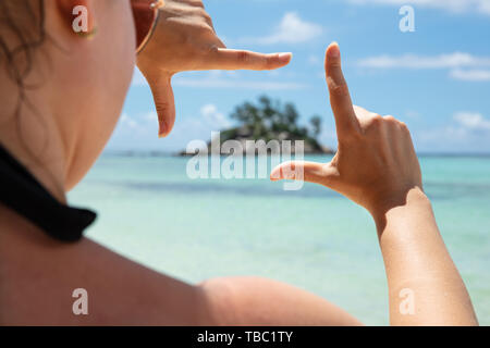 Close-up Of A Woman Making Hand Frame In Front Of Island On The Sea Stock Photo