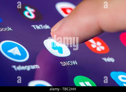 Finger pressing an icon on a smartphone or tablet touchscreen to load the Snow camera app, an image messaging and multimedia social media application. Stock Photo