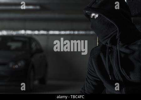 Men in Black Mask is About to Steal Modern Car on a Parking Lot. Illegal Activity Conceptual Photo. Stock Photo