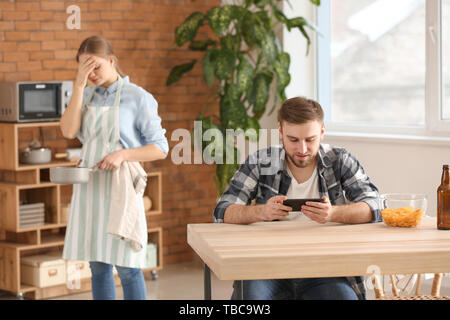 Lazy husband using mobile phone while his tired wife doing chores Stock Photo