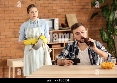 Lazy husband using mobile phone while his wife doing chores Stock Photo