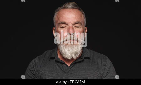 Close up of a senior man with a white beard with his eyes closed. Portrait of a senior man isolated on black background with closed eyes. Stock Photo