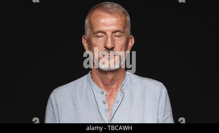 Close up of an old man with his eyes closed. Portrait of a senior man against black background. Stock Photo