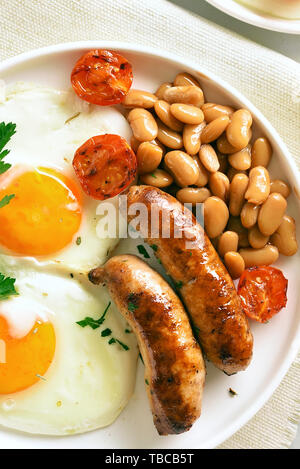 Close up of fried eggs, sausages, beans, tomatoes, greens on plate. Tasty dish for breakfast. Top view, flat lay