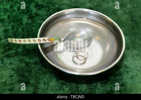 Wedding rings in the bowl with water is an Islamic custom for the sacred Karan. Stock Photo