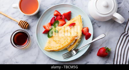Crepes, thin pancakes with cream cheese, ricotta and fresh strawberries. Marble background. Top view. Stock Photo