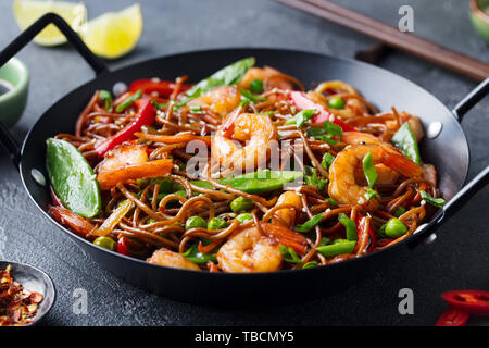 Stir fry noodles with vegetables and shrimps in black iron pan. Slate background. Close up. Stock Photo