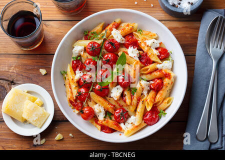 Pasta penne with roasted tomato, sauce, mozzarella cheese. Top view. Wooden background. Stock Photo