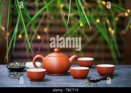 Green tea in tea pot and chawan bowls, cups. Outdoor background with bamboo leaves and bokeh lights. Copy space. Stock Photo