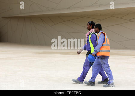 Doha, Qatar - 11 April, 2019: Two workers in uniforms with helmets walk around The National Museum of Qatar. Stock Photo